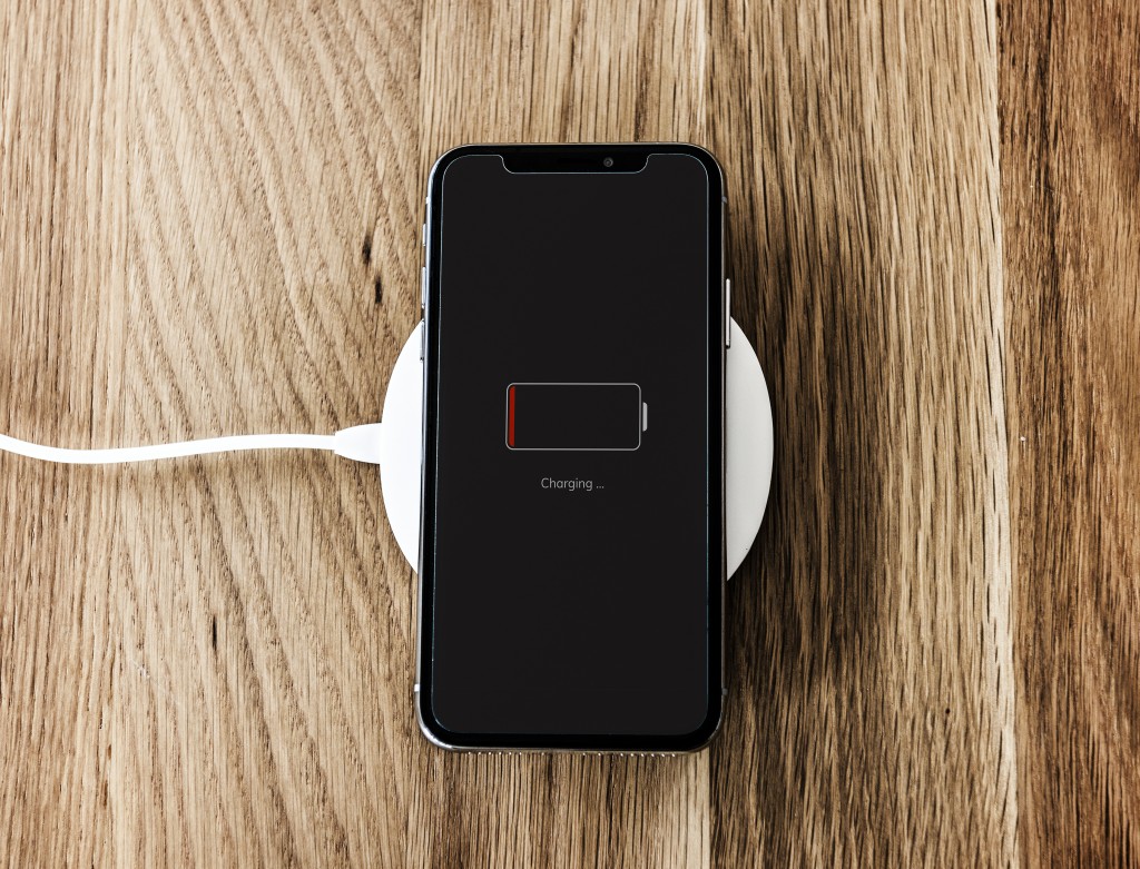 technology fix for wireless charging black cell phone low on battery laying on white charger